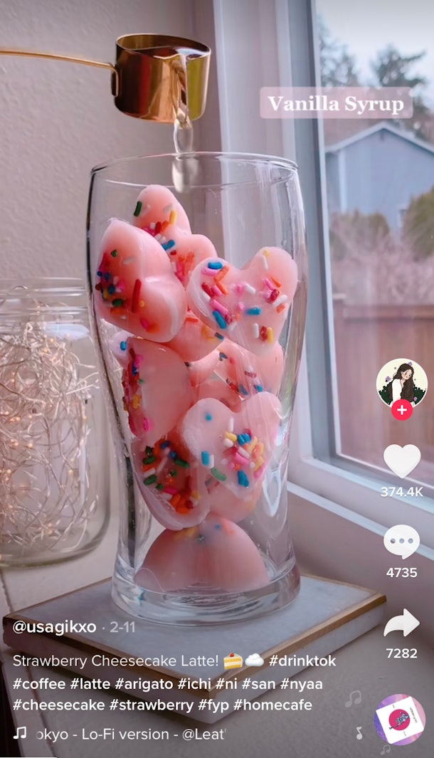 A woman makes a strawberry cheesecake latte for TikTok with pink heart strawberry ice cubes with sprinkles inside. 